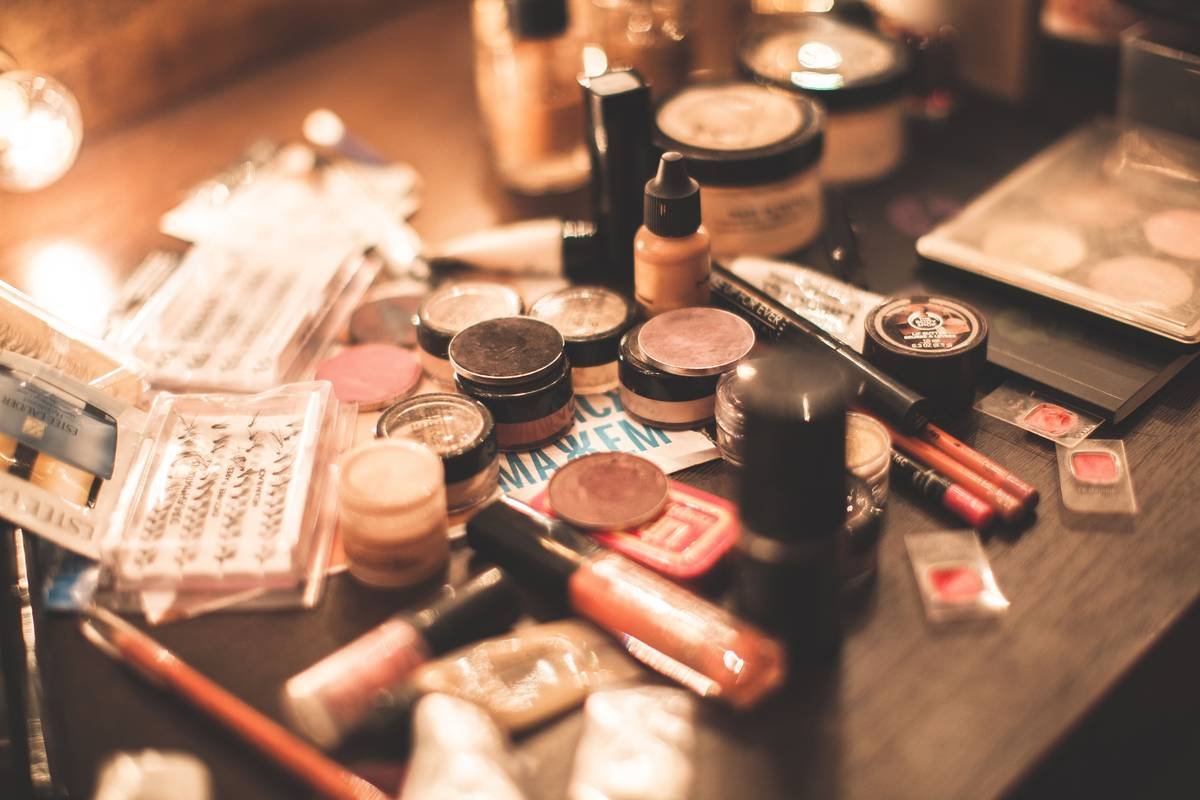 Side-by-side photo: left shows chaotic makeup drawer with spilled powders and tangled brushes; right shows same drawer organized with clear acrylic dividers holding lipsticks, eyeshadows, and liners neatly
